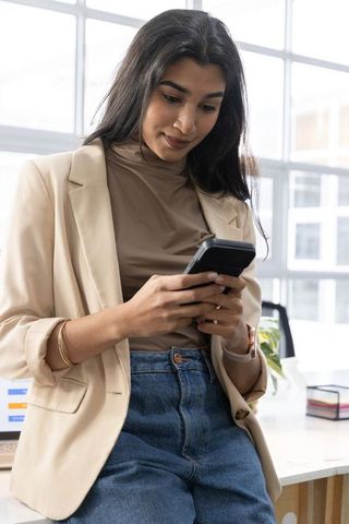 Young indian professional checking smartphone while leaning on modern office desk