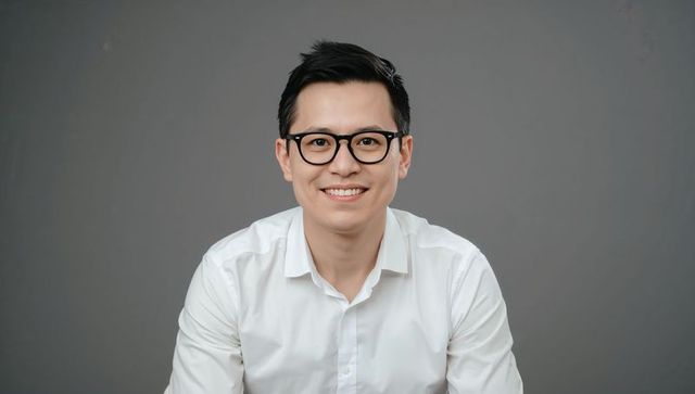 Confident young professional smiling in white shirt and black glasses studio headshot