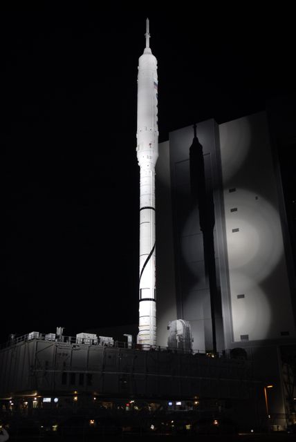 This image shows the Ares I-X rocket moving away from the Vehicle Assembly Building at NASA's Kennedy Space Center in Florida. The 327-foot-tall rocket is being transported to Launch Pad 39B atop a crawler-transporter during the nighttime. The Ares I-X is a test vehicle for the Ares I, part of NASA's Constellation Program. This photo can be used for topics related to space exploration, NASA missions, rocket technology, and aerospace engineering.