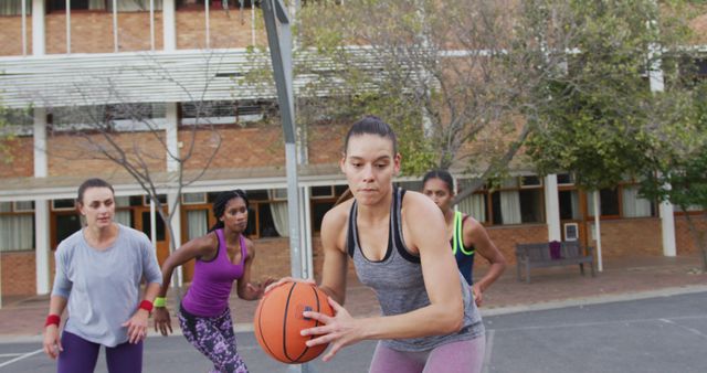 Diverse female basketball team playing match, dribbling ball. basketball, sports training at an outdoor urban court.
