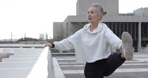 Senior woman stretching leg on rooftop rail doing urban morning exercise and warmup