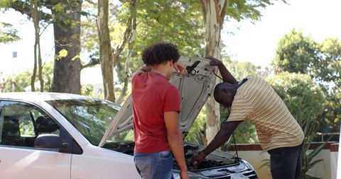 Friends collaborating on car repair in sunny driveway