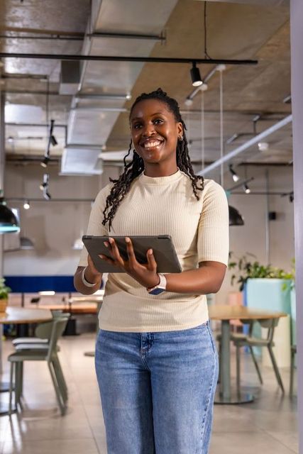 Confident african american woman holding tablet and smiling in modern coworking space