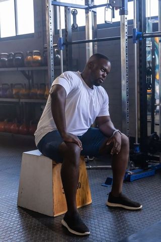 Focused african american man sitting on box leaning forward in gym post-workout recovery