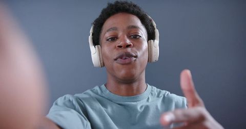Talking young man wearing beige headphones reaching forward for vlogging and streaming