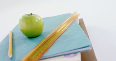 Green apple on books with pencil and ruler symbolizing education