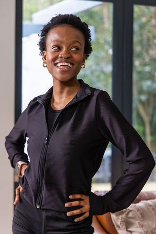 Confident african american woman in black activewear wearing smartwatch smiling near glass doors