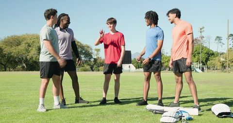 Young cricket players standing on grassy field chatting with pads bat and smartphone