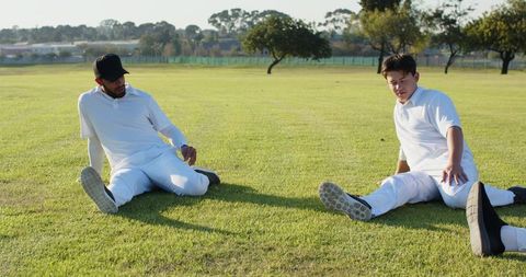 Cricket teammates stretching on sunlit grass field preparing for match