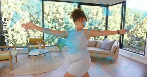 Woman practicing yoga and balancing in bright minimalist living room with large windows