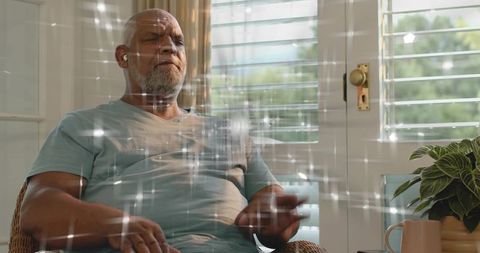 Senior man relaxing with earbuds in sunroom, meditating in cozy sunlit interior