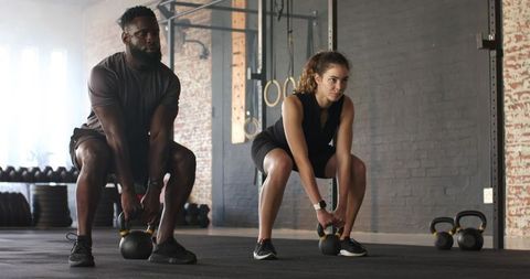 Focused fitness duo engaging in kettlebell squats in modern gym