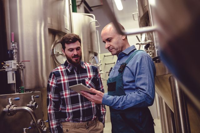 Low angle view of worker and owner discussing over digital tablet at brewery