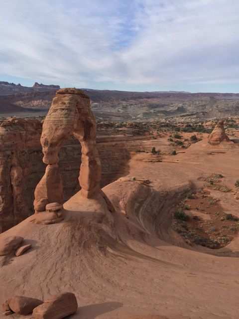Majestic Delicate Arch standing under a partly cloudy sky in Arches National Park with expansive desert stretching beyond. Perfect for travel blogs, nature websites, educational materials about geology, tourism promotions, and adventure-themed campaigns.