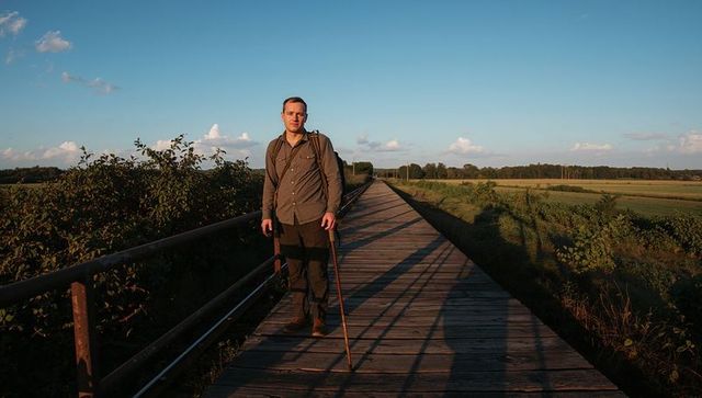 Solo hiker walking on wooden boardwalk at golden hour carrying backpack and walking stick