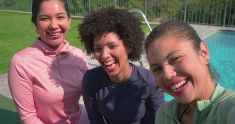 Three women laughing and taking selfie at backyard pool in pastel activewear on sunny day