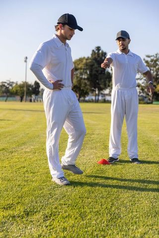 Multicultural cricket teammates practicing footwork drills on green turf with coach guidance