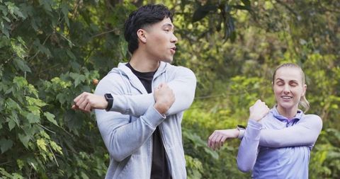 Couple stretching shoulders on outdoor trail with smartwatches