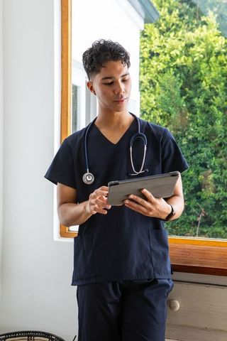 Asian Male Doctor in Navy Scrubs Using Tablet by Window