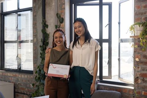 Diverse Female Coworkers Holding Certificate in Modern Office