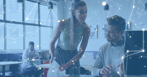 Young professionals collaborating at monitor with digital network overlay and charts