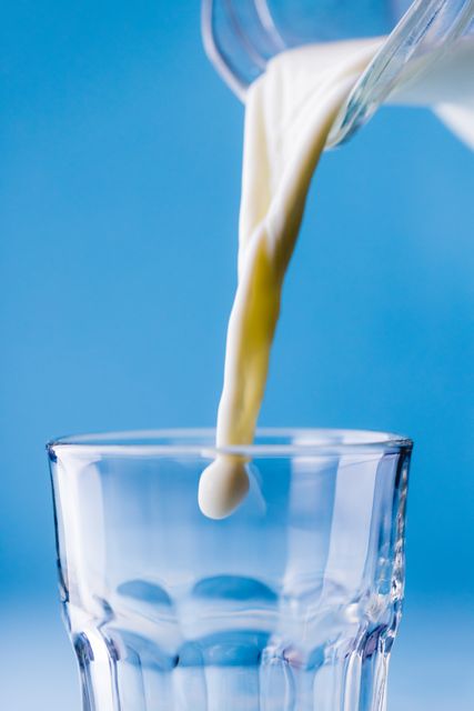 Close-up of milk being poured in jug against blue background, copy space. unaltered, food, drink, studio shot and healthy eating.
