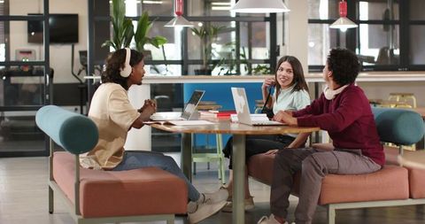 Young African American coworkers collaborating around table in modern coworking space with laptops