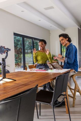 Diverse creators filming lifestyle tutorial at sunlit dining table with phone gimbal