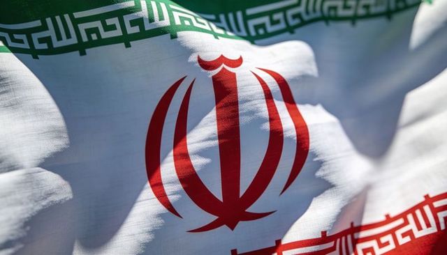 Waving iranian flag close-up showing red emblem on sunlit tricolor fabric