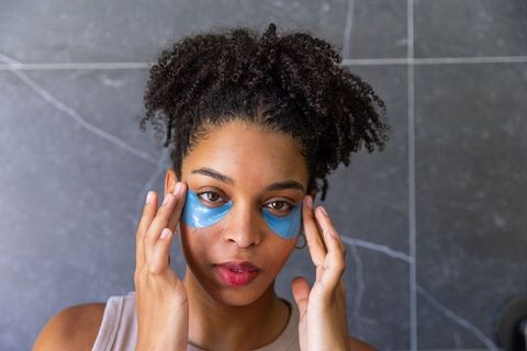 African american woman applying blue gel under-eye patches and massaging temples