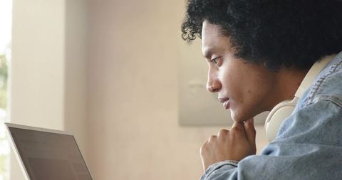 African american man studying on laptop with headphones, concentrating at home desk