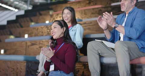 Diverse audience clapping and smiling on tiered bench seating at modern conference event