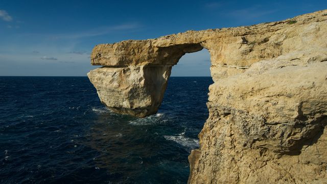 This stock photo depicts the Azure Window, a famous natural limestone rock arch over the Mediterranean Sea. Known for its striking beauty and geological significance, it features rugged cliffs and deep blue waters. Perfect for travel guides, nature documentaries, educational materials on geology, and websites promoting tourism in Malta. Also suitable for use in brochures, posters, and backgrounds that require stunning natural landscapes.