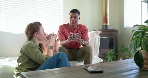 Sharing morning coffee and conversation on sofa, diverse couple connecting at home