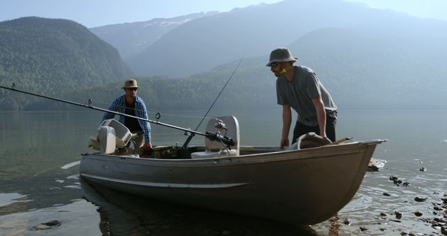Two middle-aged Caucasian men are preparing for a fishing trip on a serene lake, with copy space. One man is seated at the stern handling the fishing rod, while the other stands steadying the boat.
