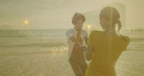 Golden-hour lovers dancing on beach with dreamy double-exposure city lights and waves