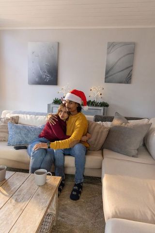 Couple cuddling on beige sectional sofa wearing santa hat cozy holiday home togetherness