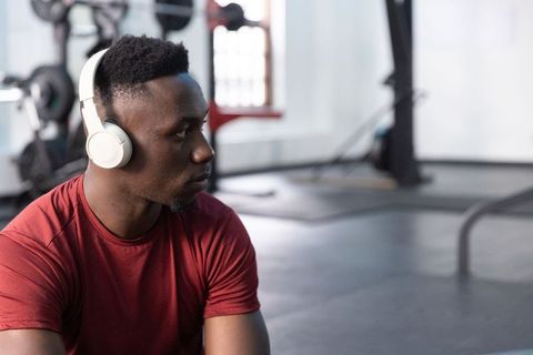 African american man resting in gym wearing headphones and red shirt for fitness lifestyle