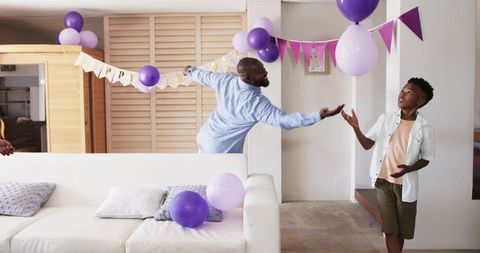 African American father and son decorating living room with purple balloons and bunting