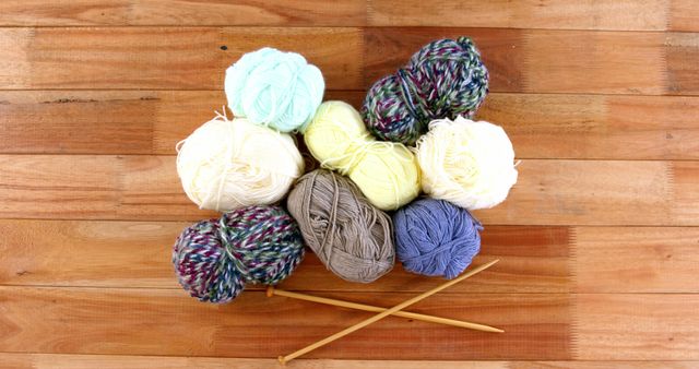 Colorful balls of yarn and a pair of knitting needles are arranged on a wooden surface, with copy space. This setup suggests a crafting theme, for knitting or crochet enthusiasts.