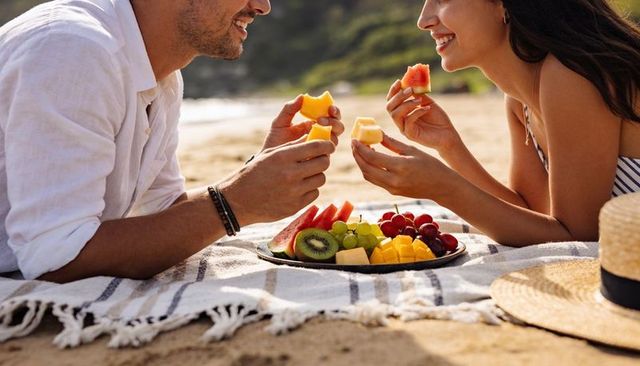 Couple sharing fresh fruit picnic on sunny beach romantic seaside summer moment