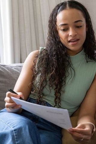 Young african american woman reviewing documents on couch working from home