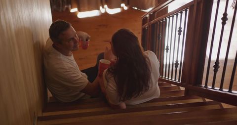 Couple relaxing on stairs sharing coffee at home