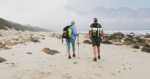 Senior couple trekking on misty beach with backpacks