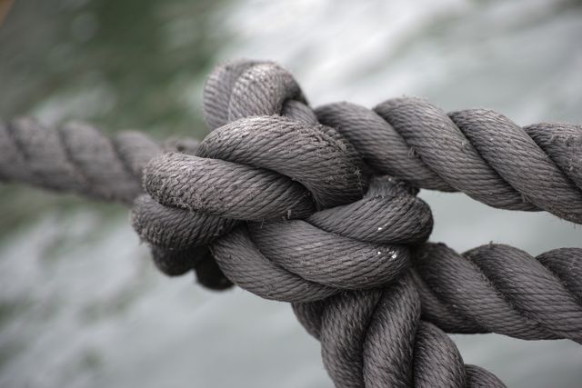 This image shows a close-up view of a thick marine rope tied in a strong knot over water. The texture and strength of the rope are clearly visible, suggesting sturdiness and reliability. Ideal for use in articles or presentations related to boating, nautical activities, maritime industry, and securing heavy loads. Suitable for illustrating concepts of strength, durability, and marine equipment.