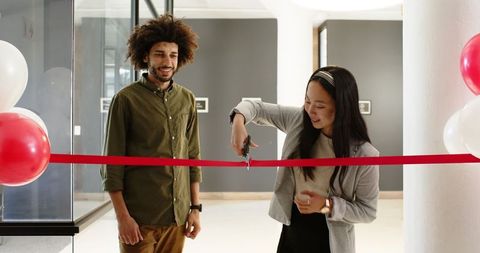 Businessman and businesswoman cutting ribbon at office opening
