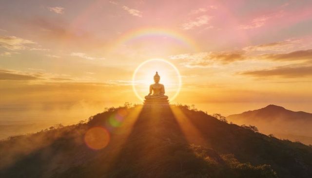Golden buddha radiating halo and sunbeams on mountain summit at misty sunrise