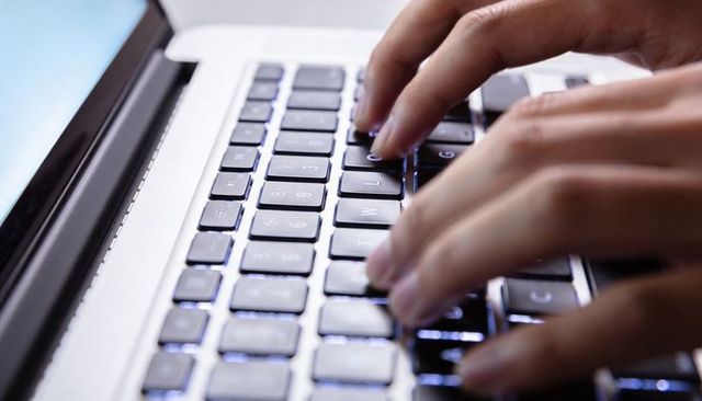 Typing on Backlit Laptop Keyboard Showing Silver Chassis, Blue Glow and Focused Fingers