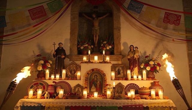 Candlelit chapel altar with crucifix, madonna and friar statues, marigold offerings