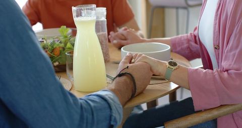 Couple holding hands across casual dining table with lemonade carafe salad and warm morning light